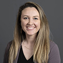 Kayla is pictured from the shoulders up. SHe has long brown/blonde hair, pale skin, and is smiling. 