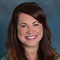 Sara is pictured from the neck up. She has long brown hair, pale skin and is smiling. 