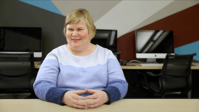 Play video featuring Sarah sitting in a computer lab with her hands on the table.