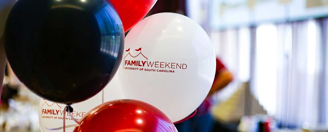 Red, black, and white balloons with “Family Weekend, University of South Carolina” printed on them, displayed indoors during an event