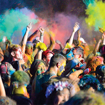 Large gathering of people at a color run covered in colored chalk dust and clouds of it in the air.