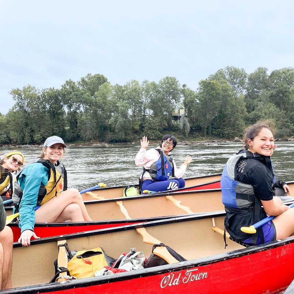 Several people wearing life jackets in canoes floating on a lake and smiling at the camera.