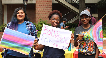 Three students smiling holding LGBTQ+ flags they made.