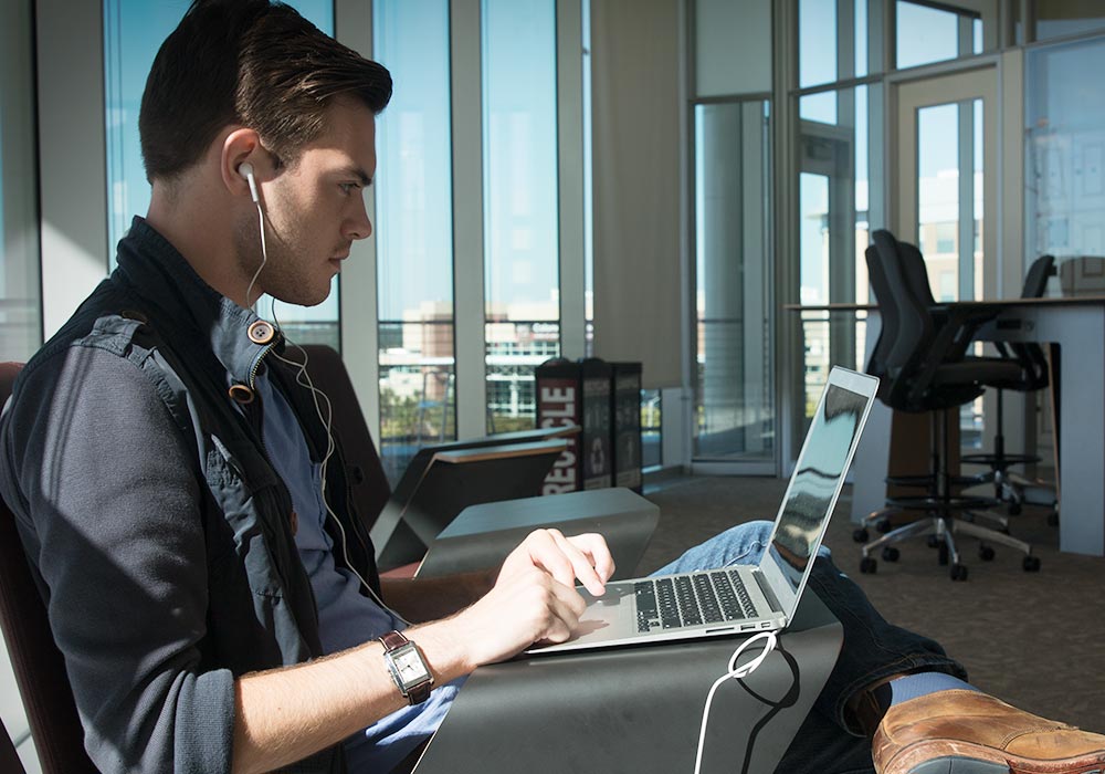 Student working on a laptop wearing earbuds.