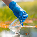 Hand holding beaker above fresh water pond