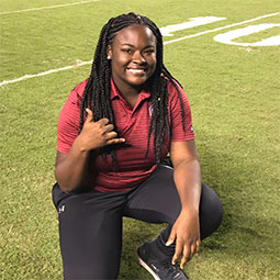 Lyric Swinton Lyric Swinton kneels on a football field and gives the spurs up hand signal