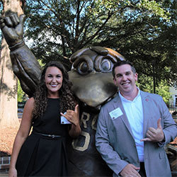 Tara Parker and Blake Edmunds stand with the bronze statue of Cocky giving the spurs up hand signal
