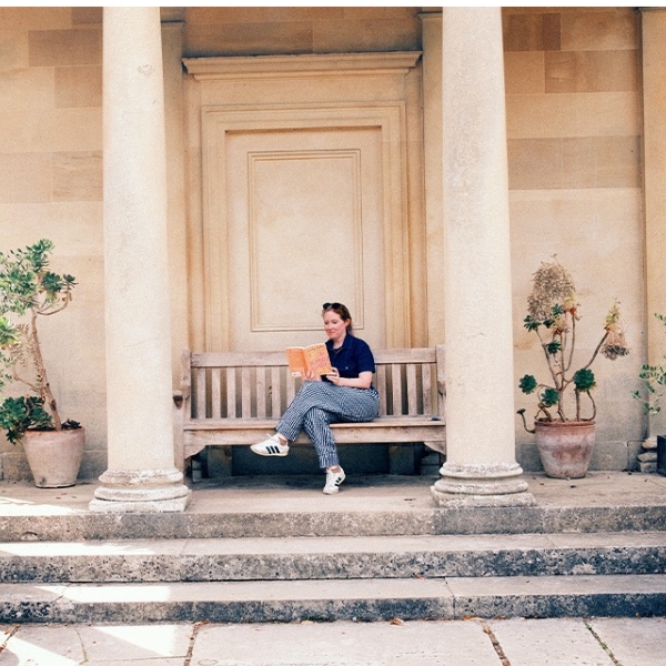 Ashley Poston sits on a bench in an English garden and reads a book. 