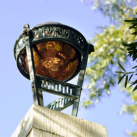 Historic ornamental amber glass globe and decorative green metal framework on the Maxcy Monument at the University of South Carolina, photographed against a clear blue sky with tree foliage in the background