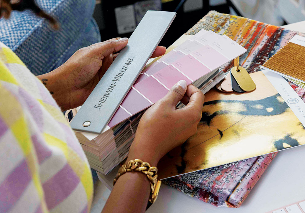 Amber Guyton (hands view) looks through Sherwin-Williams paint color swatches.